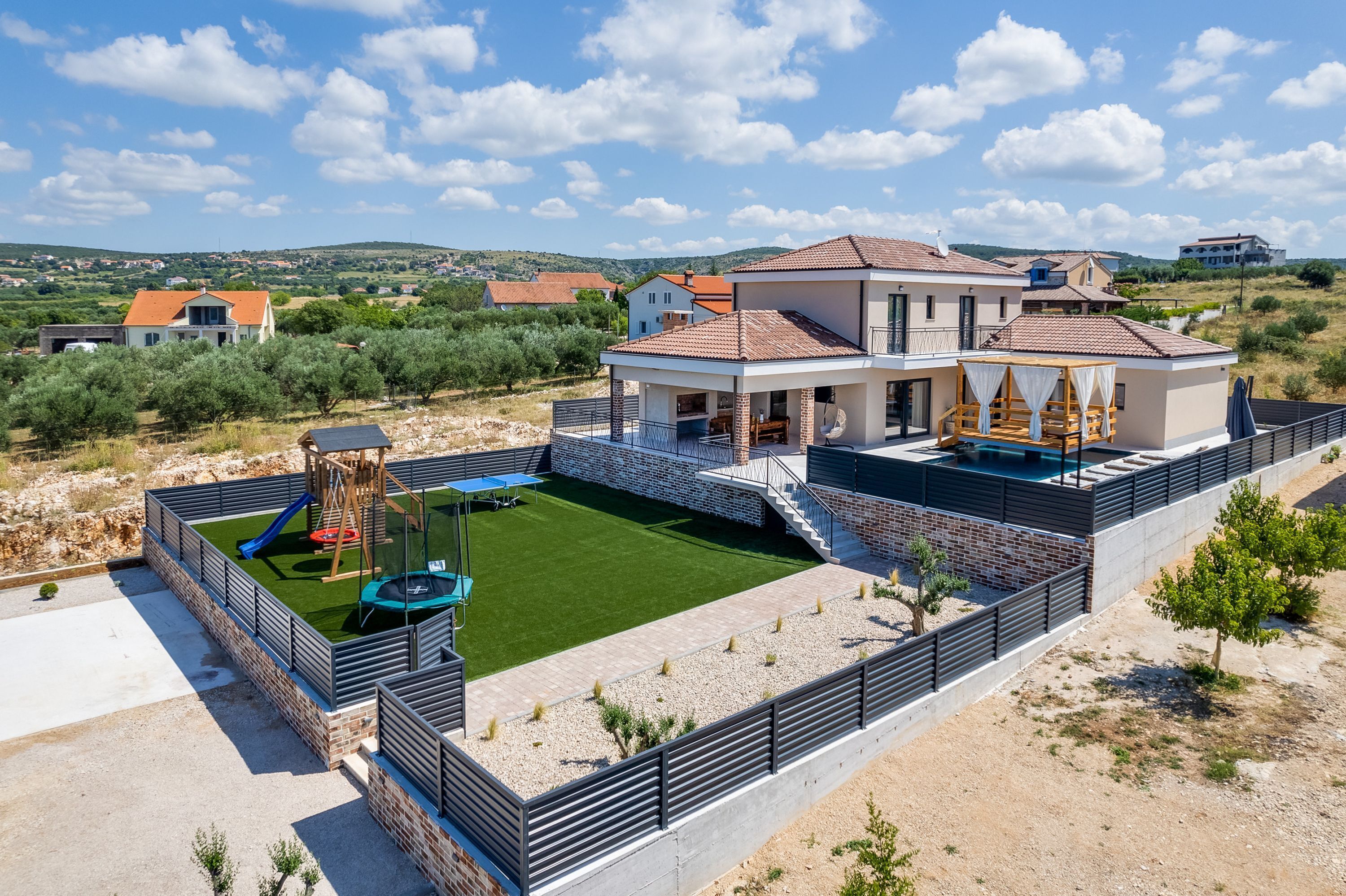 A modern two-story house with a patio, a play area, and a view of the surrounding landscape.
