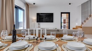 A modern dining area with a large table set for six, a bottle of wine, and candles. A flat-screen TV is mounted on the wall above the table. - Villa Alba Zadarvillas (Pakostane)