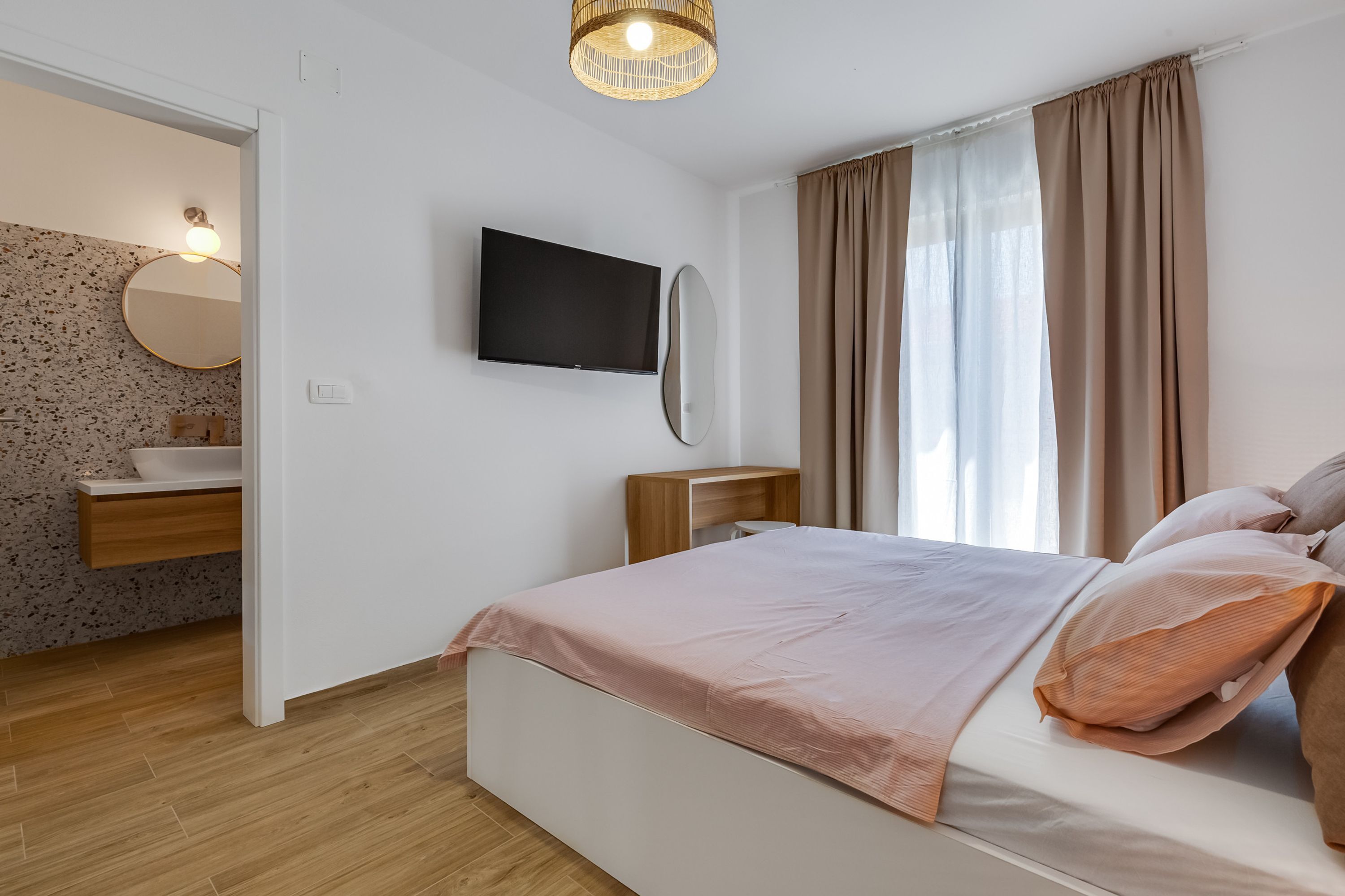 A bedroom with a bed, a TV, a mirror, and a window with curtains.