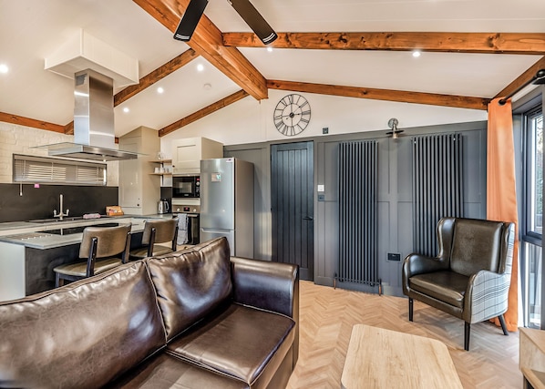 A modern kitchen with a central island, a dining area with a leather sofa, and a large window with curtains. - 1 bedroom accommodation in Snitterfield, Stratford Upon Avon (Snitterfield, Stratford Upon Avon)