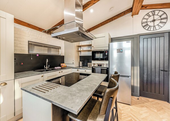 A modern kitchen with a central island, stainless steel appliances, and a wooden ceiling.