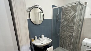 Ein Badezimmer mit Waschbecken, Spiegel, Dusche und Waschmaschine.