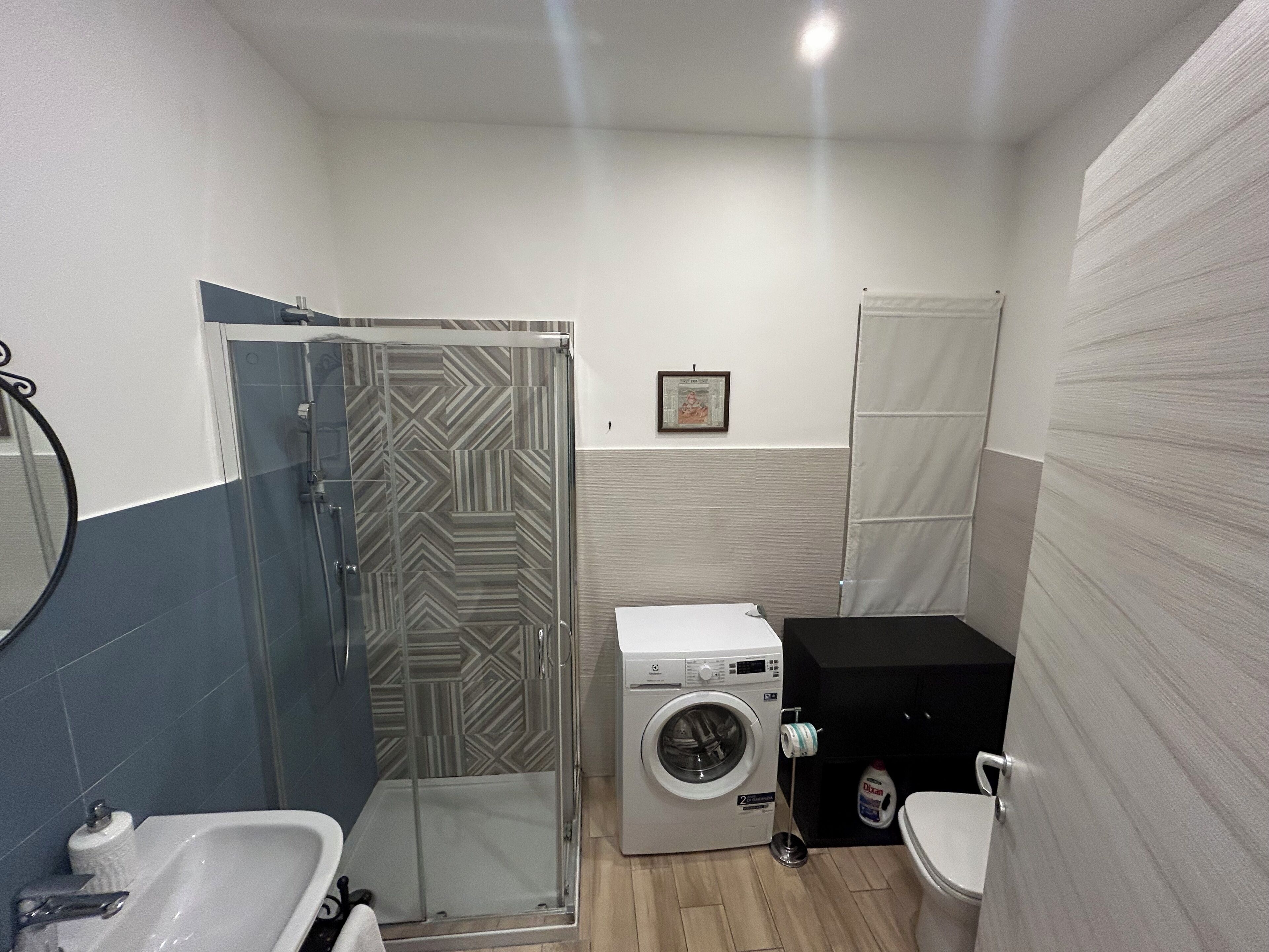 Et lille badeværelse med bruser, vaskemaskine, toilet og håndvask.