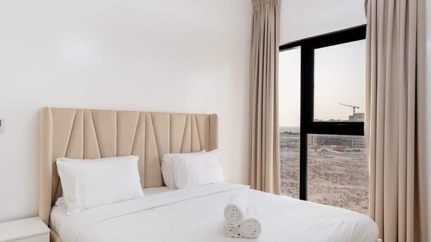 Quarto de hotel com uma cama grande, uma mesa de cabeceira e vista para uma construção através de uma janela ampla.
