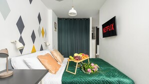 Une chambre d’hôtel bien rangée, avec un lit, une table de chevet dotée d’une lampe, un téléviseur fixé au mur et un rideau.