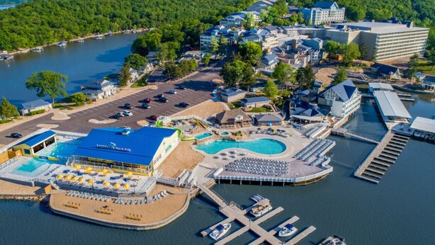 Vue aérienne d’un complexe hôtelier doté d’une grande piscine, d’un port de plaisance où sont amarrés des bateaux, et de différents bâtiments, dont un hôtel et un centre de conférences.