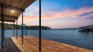 Une terrasse en bois avec une rambarde en métal, un espace abrité et une vue sur un lac avec un quai.