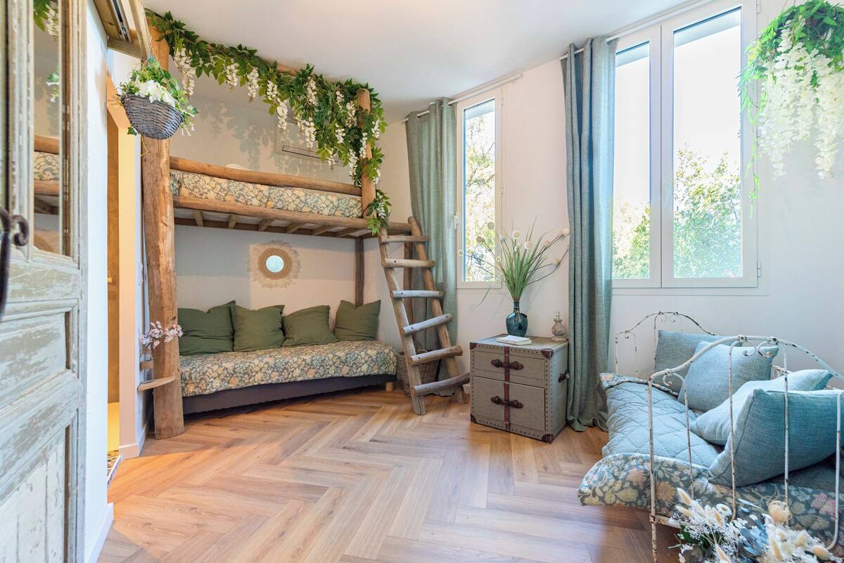 Une chambre avec un lit superposé, une échelle, une petite table avec des tiroirs et une plante suspendue.