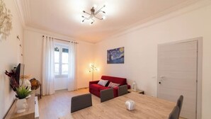 A modern living room with a wooden dining table, red sofa, and a painting on the wall. - Elegant and spacious apartment 100 meters from Bracciano Station (Bracciano)