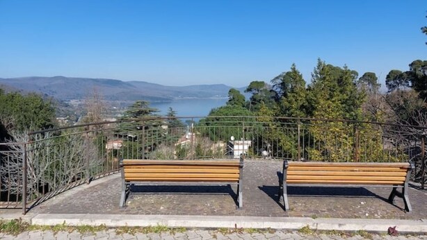 Two wooden benches on a paved area with a metal railing, overlooking a body of water and distant hills. - Elegant and spacious apartment 100 meters from Bracciano Station (Bracciano)