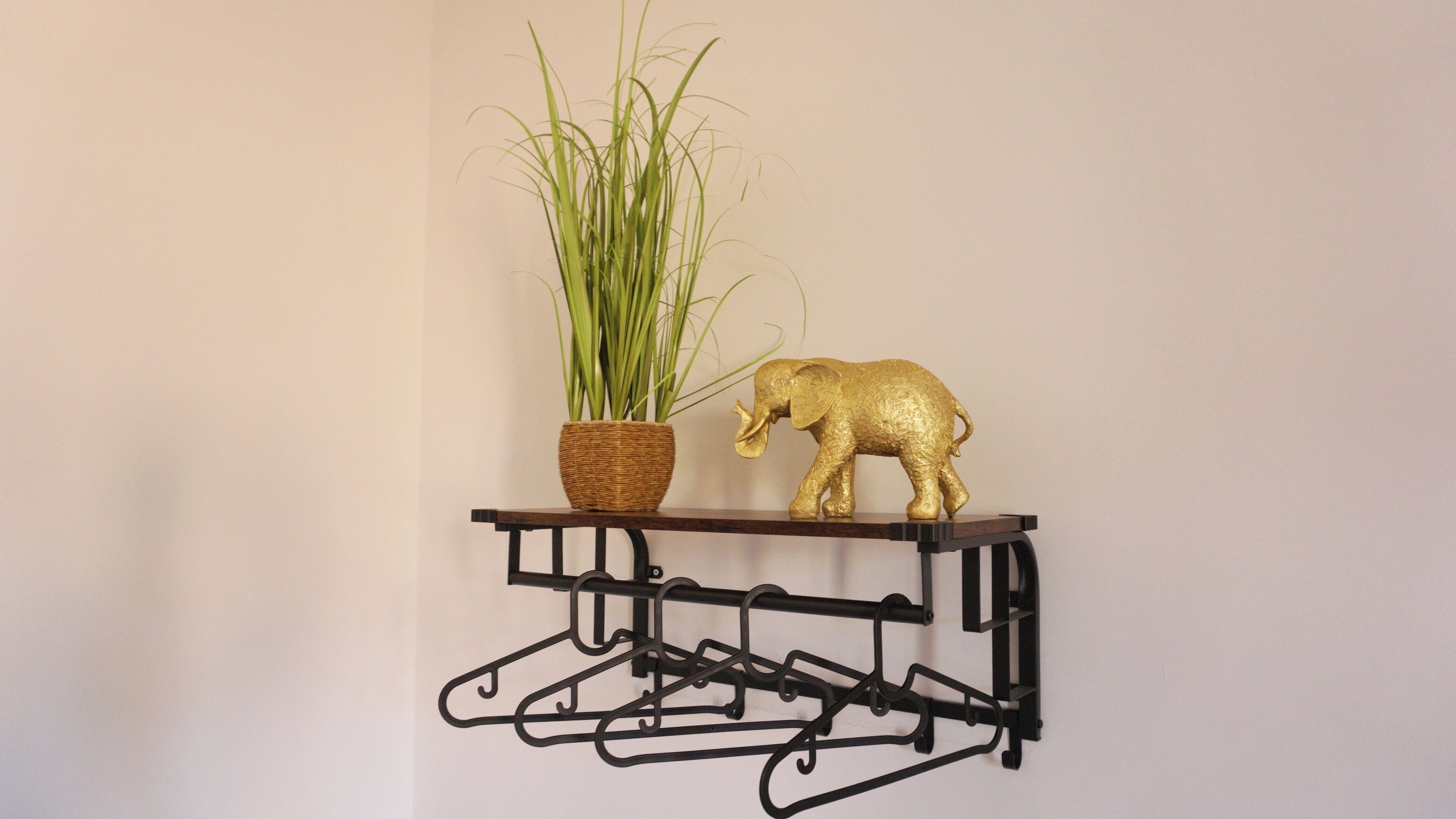 A wall-mounted shelf with a plant and a golden elephant figurine.
