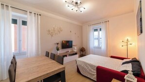 A modern bedroom with a bed, a red sofa, a wooden table, and a TV on a stand. - Elegant and spacious apartment 100 meters from Bracciano Station (Bracciano)