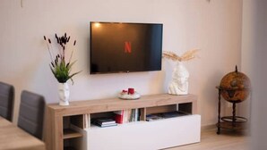 A modern living room with a flat-screen TV mounted on a wooden console, a globe on a stand, and a vase with plants. - Elegant and spacious apartment 100 meters from Bracciano Station (Bracciano)