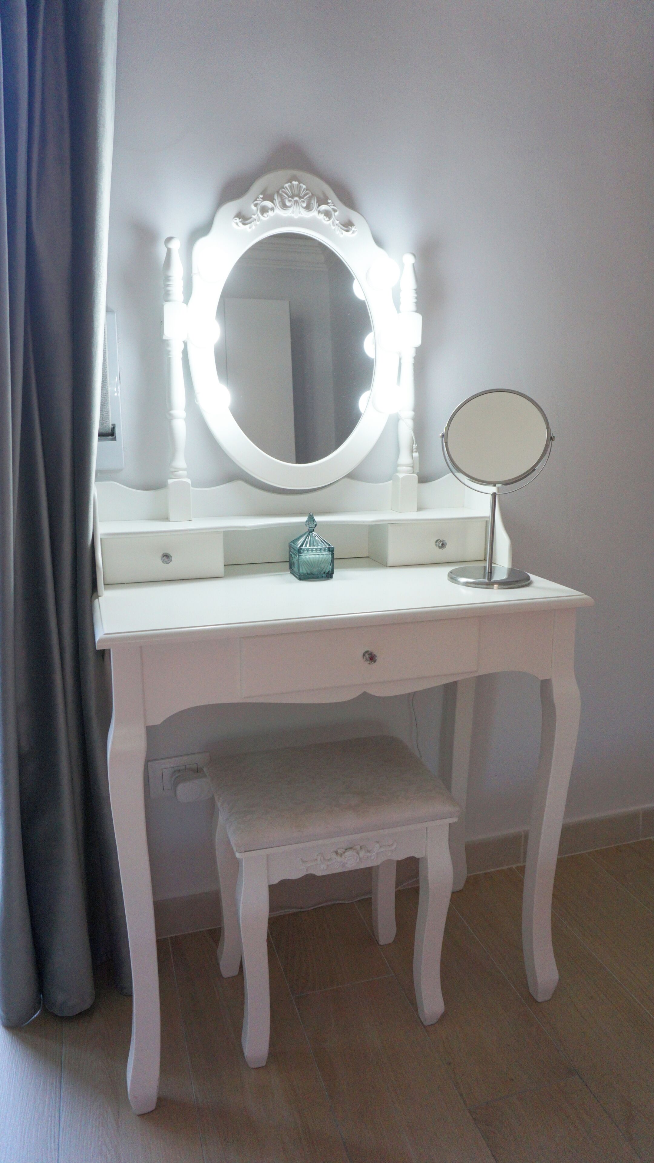 A white vanity with a round mirror, a smaller round mirror, and a decorative glass container.
