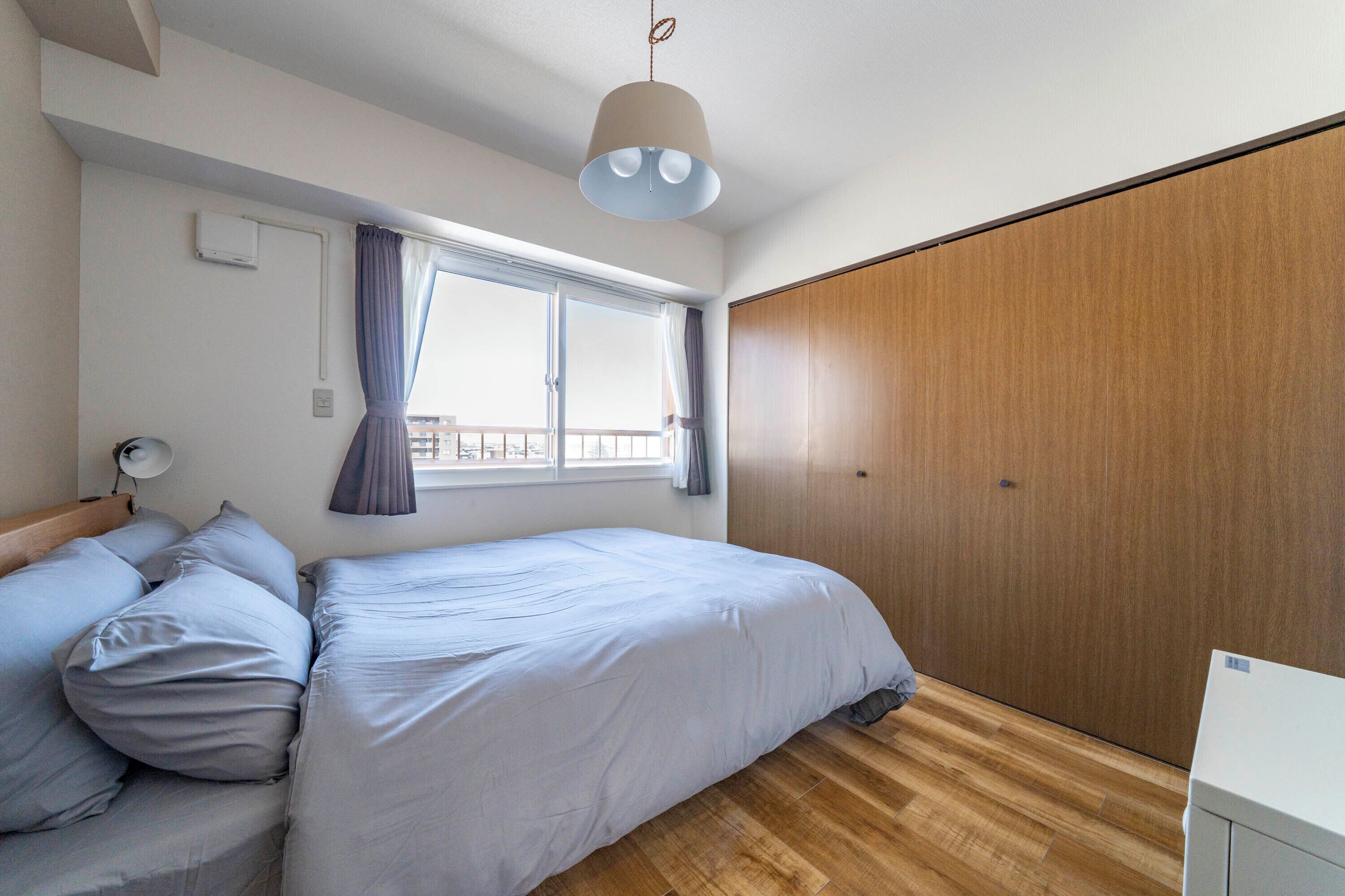 A bedroom with a bed, a bedside table, a lamp, a window with curtains, and a wardrobe.