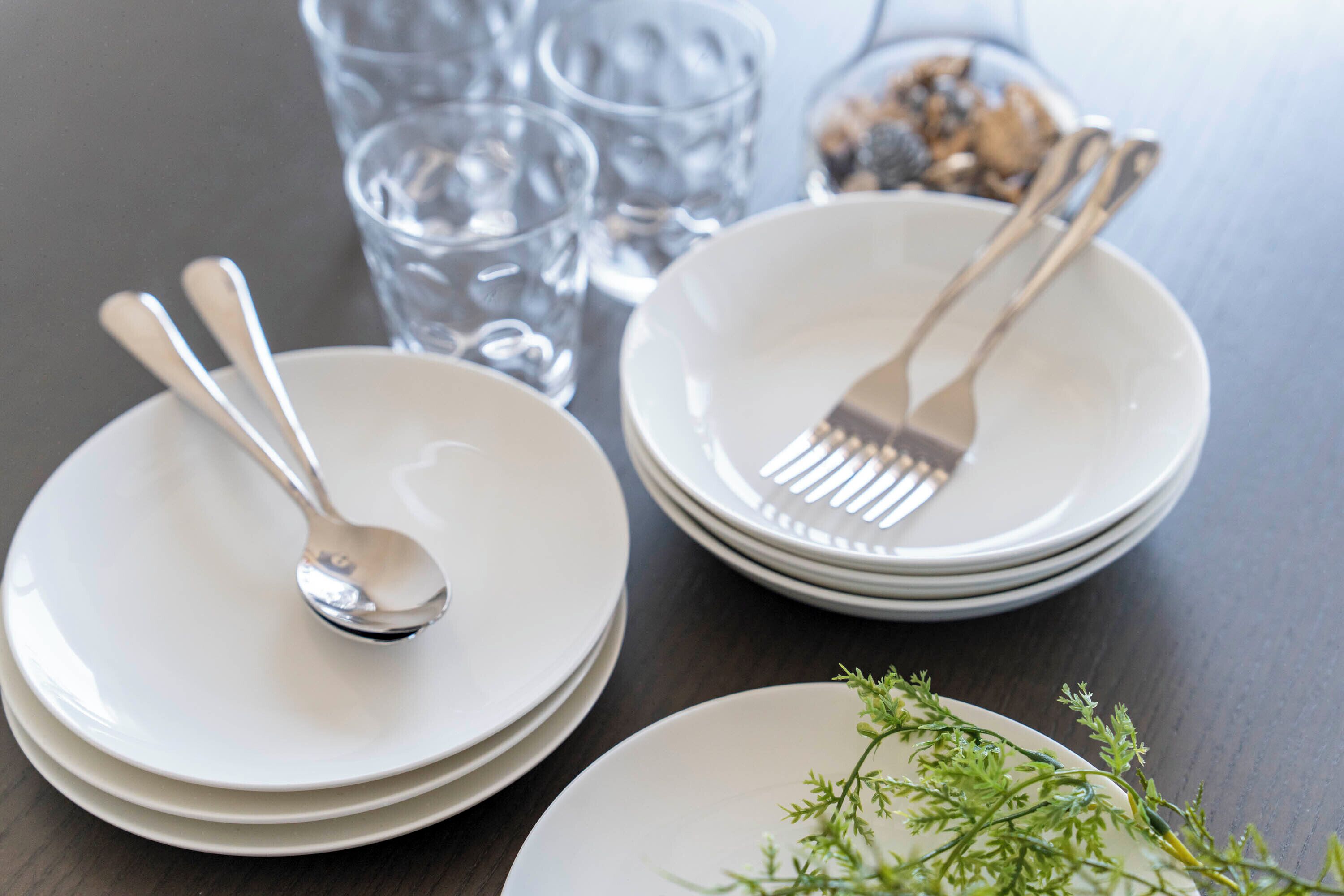 A table with stacked white plates, a fork, and a spoon.