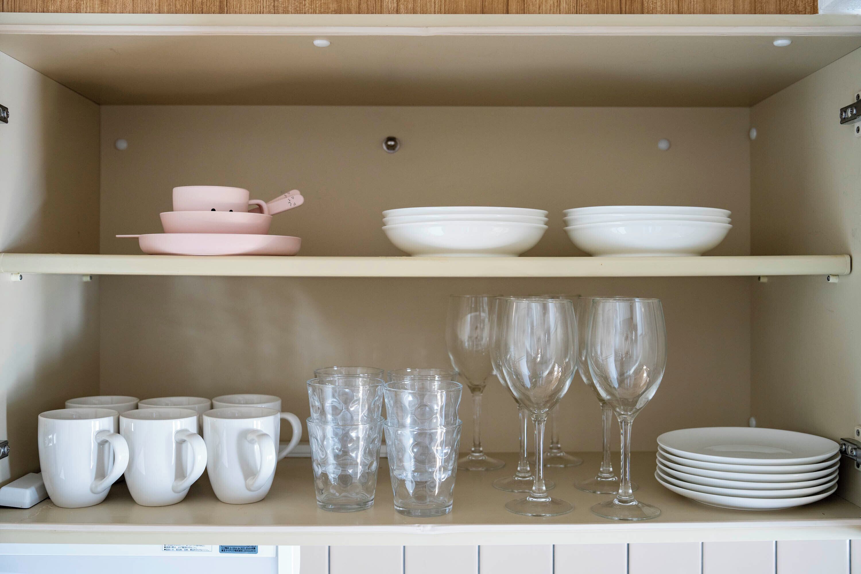 A kitchen shelf with white mugs, clear glasses, and white plates.