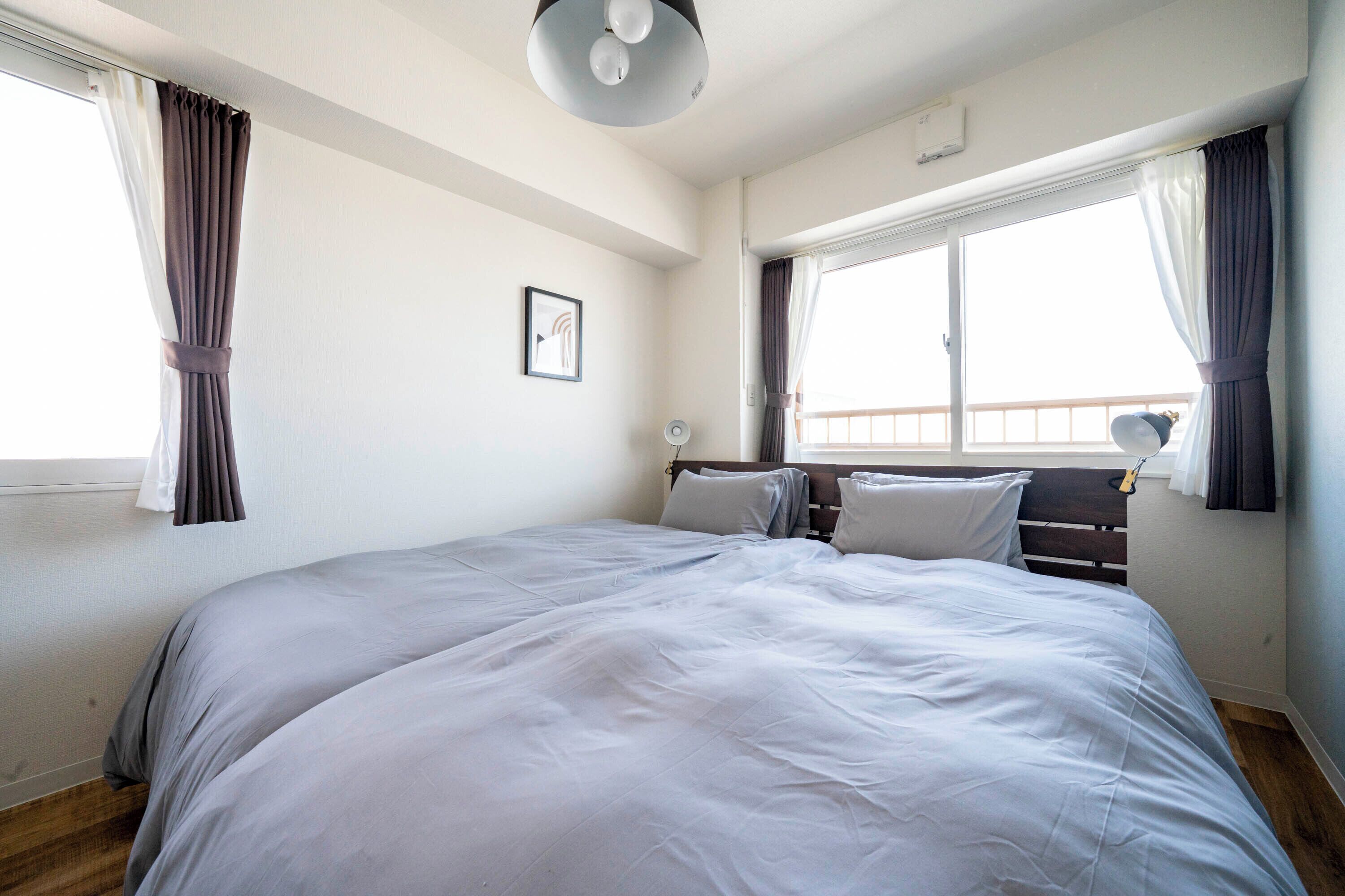 Ein Schlafzimmer mit einem großen Bett, zwei Nachttischen, einer Deckenleuchte und einem mit Vorhängen versehenen Fenster.