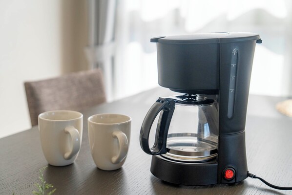 Una cafetera sobre una mesa con dos tazas blancas a su lado.
