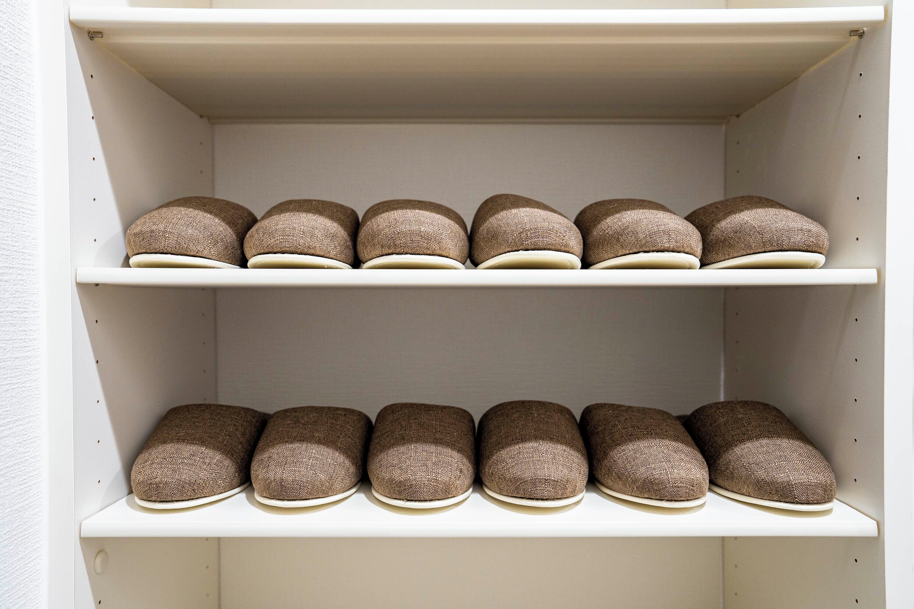 Ein weißer Schrank mit zwei Ablagen, auf denen mehrere Paare brauner Schuhe liegen.