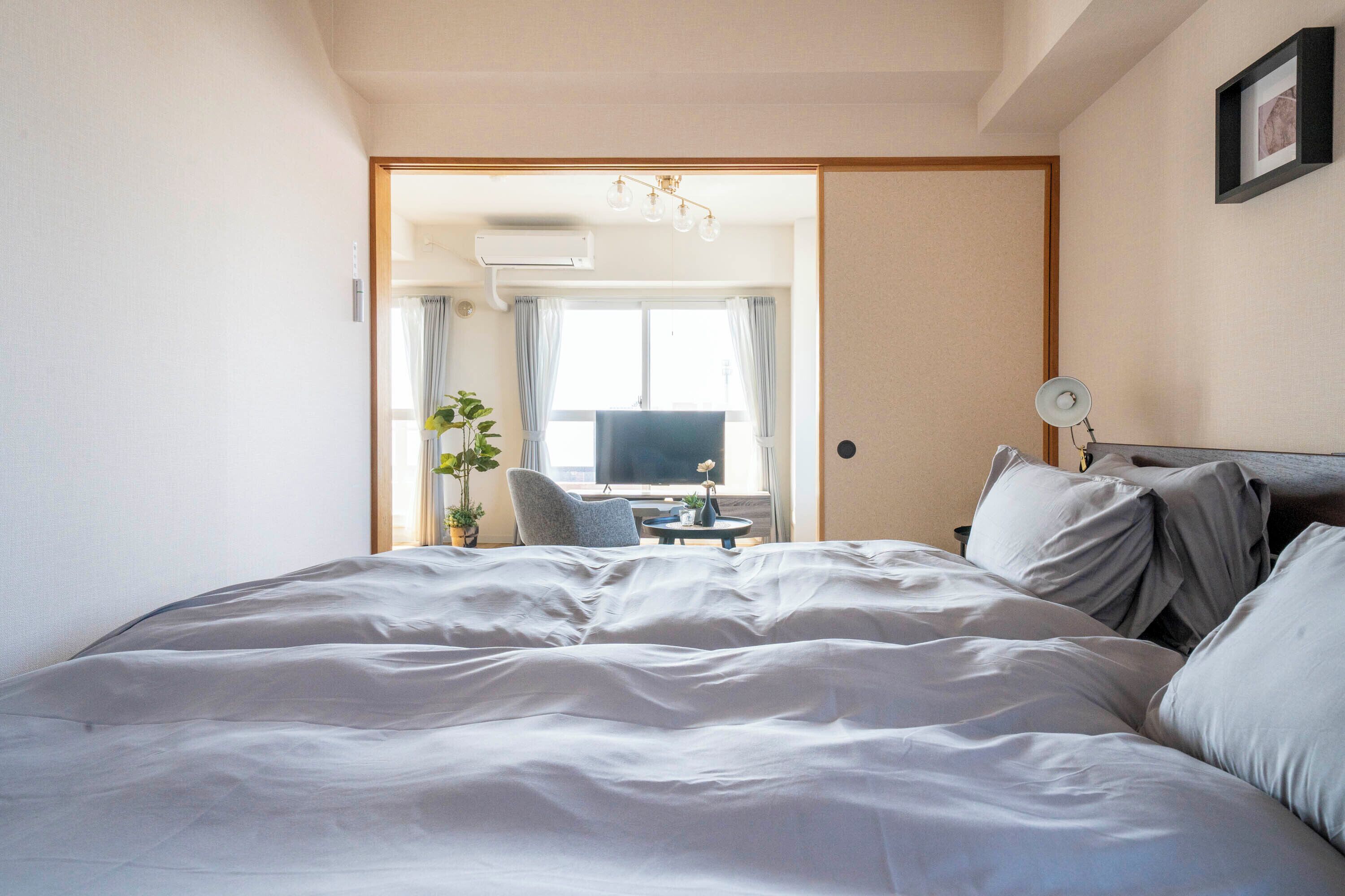 A neatly made bed with a view of a room that includes a television, a small table, and a chair.