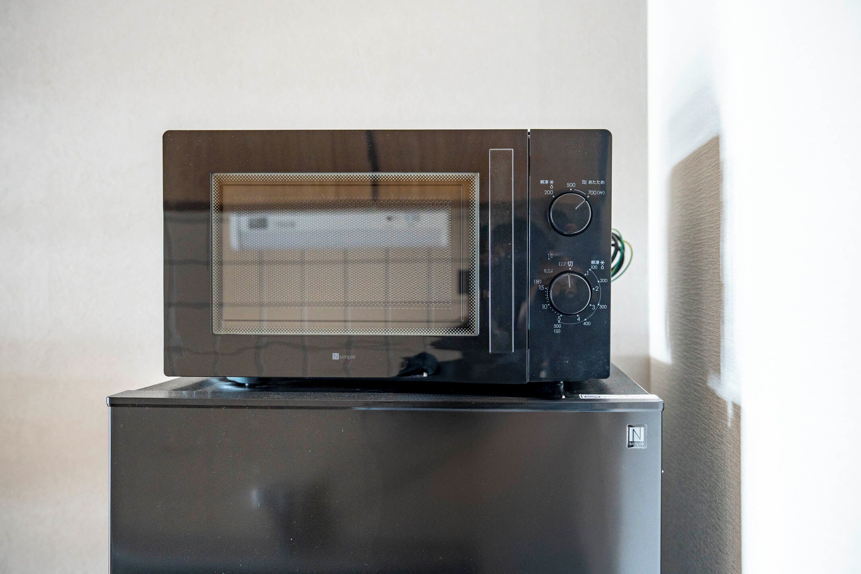 A microwave oven with a digital display and control panel on top of a refrigerator.