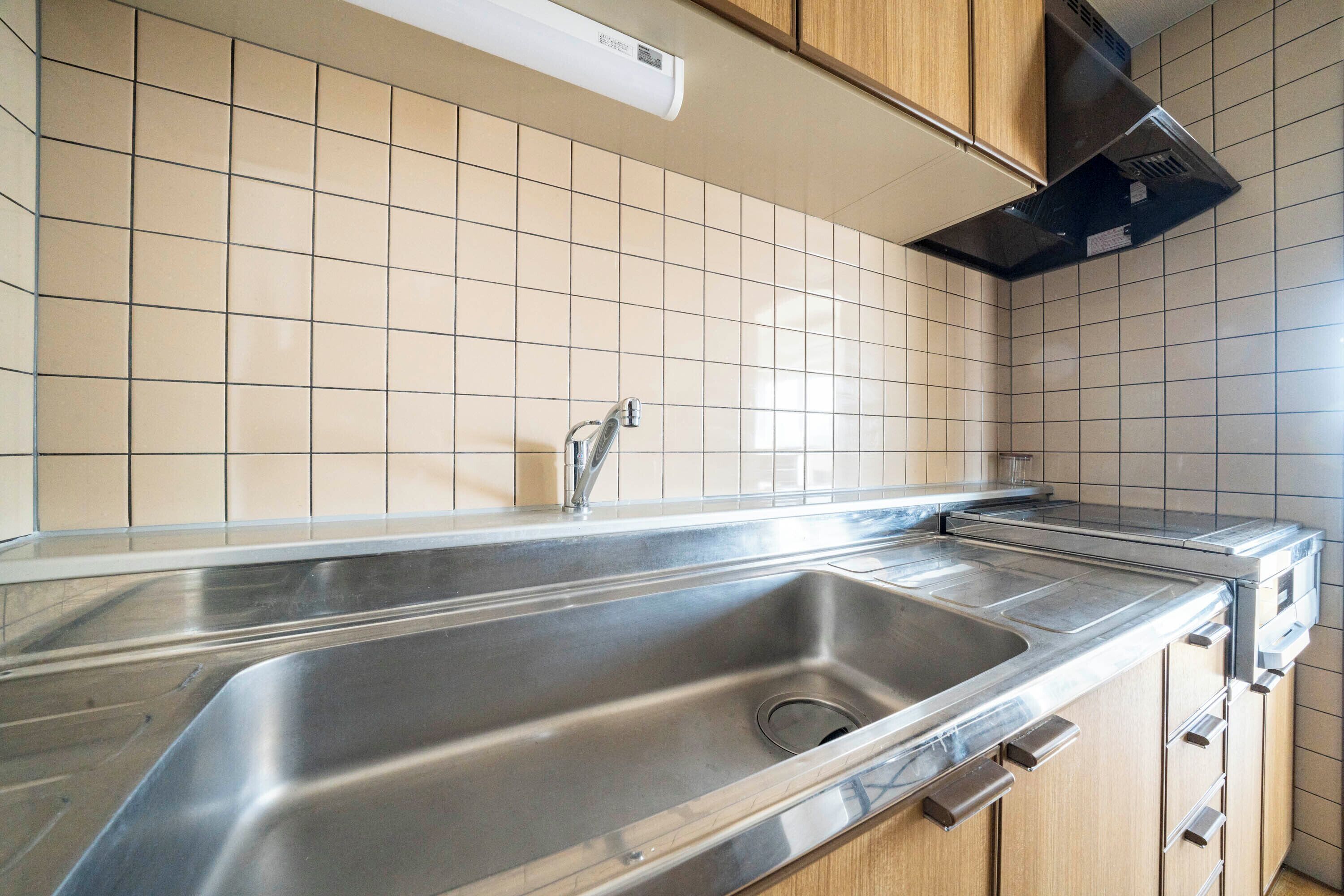 Een keuken met een RVS spoelbak, houten kastjes en een betegelde achterwand.