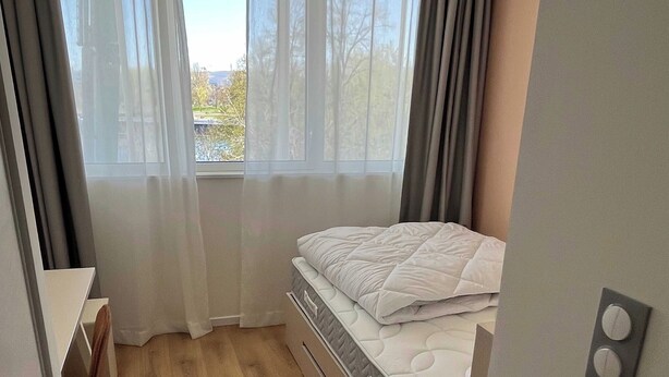 A bedroom with a bed, a desk, and a window with curtains. - Comfort Studio in a Premium Residence- Sport/cinema (Huningue)