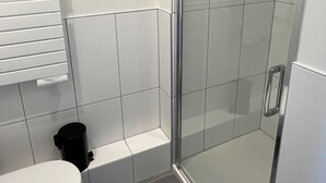 A bathroom with a toilet, a glass-enclosed shower, and a white tiled wall. - Comfort Studio in a Premium Residence- Sport/cinema (Huningue)