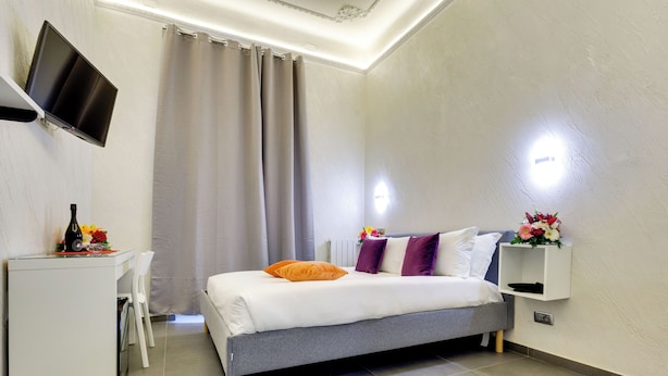 Una camera d'albergo moderna con un letto, una scrivania e un televisore fissato alla parete.