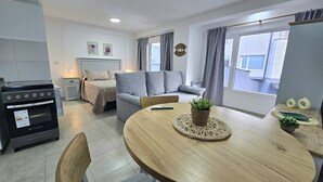 Una sala de estar moderna con un sofá, una mesa de comedor con una planta y una zona de cocina con estufa.