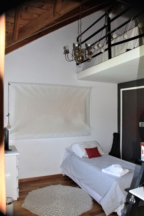 A bedroom with a bunk bed, a bedside table, a lamp, a hanging light fixture, and a window with blinds.
