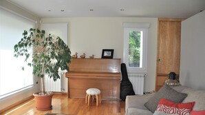 Una sala de estar con un piano de madera, un árbol en maceta, un sofá con cojines y un radiador.