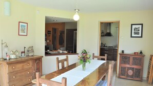 Un comedor con una mesa de madera, sillas, un jarrón con flores, un aparador y una cocina al fondo.
