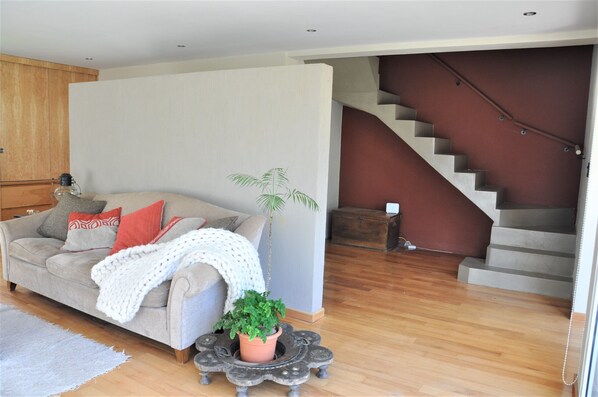 A living room with a sofa, a potted plant, and a staircase.