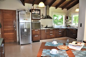 Une cuisine avec des meubles en bois, un réfrigérateur en acier inoxydable, un four à micro-ondes et une cuisinière. Une fenêtre offre une vue sur la verdure environnante.