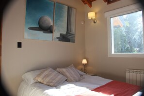 A bedroom with a bed, pillows, a painting, a nightstand, a lamp, and a window.