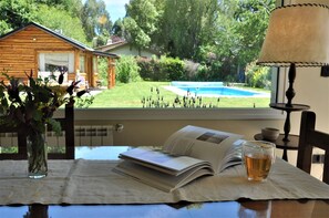 A table with an open book, a glass of amber liquid, and a vase with flowers.