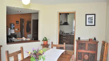 Un comedor con una mesa de madera, sillas y una planta en maceta. Se ve una cocina a través de un vano abierto.