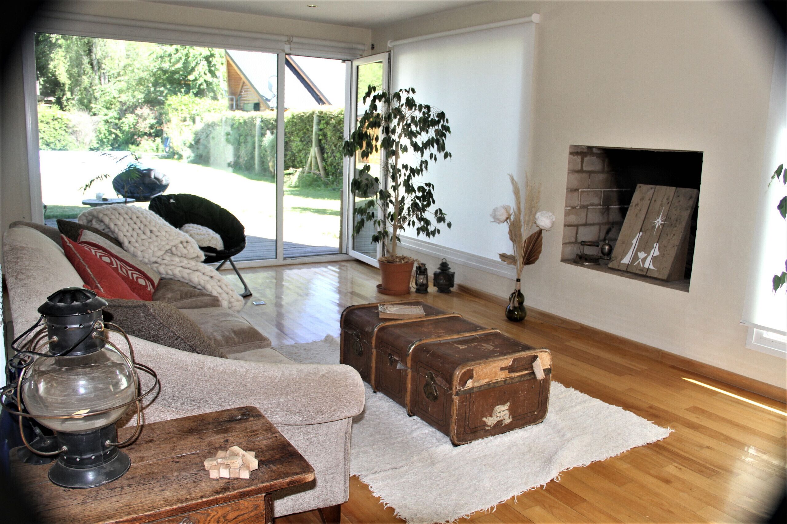 Una sala de estar con piso de madera, un sofá, una mesa con un farol, una chimenea y vistas al exterior.