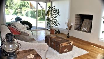 Una sala de estar con piso de madera, un sofá, una mesa con un farol, una chimenea y vistas al exterior.
