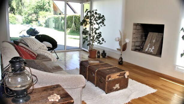 Una sala de estar con piso de madera, un sofá, una mesa con un farol, una chimenea y vistas al exterior.