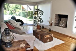 Un salon doté d’un plancher en bois, d’un canapé, d’une table avec une lanterne, d’une cheminée et offrant une vue sur l’extérieur.