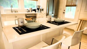 Une cuisine moderne avec des meubles blancs, un îlot central doté d’un set de table noir et deux chaises blanches.