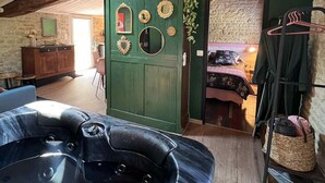 Une pièce chaleureuse avec un plafond en bois, une porte verte ornée de miroirs décoratifs, un jacuzzi noir et un lit recouvert d’une couvre-lit à motifs floraux.