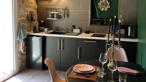 Une cuisine moderne avec des meubles de couleur sombre, une table à manger dressée pour deux personnes et une grande horloge au mur.