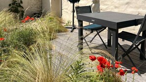 Une terrasse extérieure avec une table et des chaises, entourée de hautes herbes et de fleurs rouges.