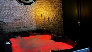 Un espace de bien-être doté d’un mur en pierre, d’un plafond en bois et d’un jacuzzi éclairé de lumières rouges.