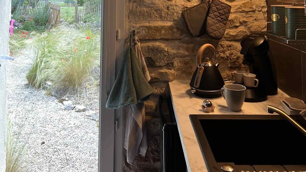 Une cuisine rustique avec un mur en pierre, un plafond en bois et une vue sur un jardin.