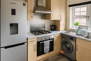 A compact kitchen with a stainless steel refrigerator, a gas stove, a built-in oven, a dishwasher, and wooden cabinets.